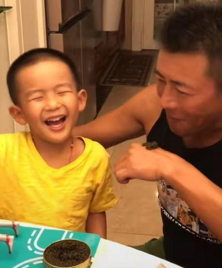 57岁高曙光与儿子吃西餐，儿子身穿黄色t恤笑眼弯弯模样可爱